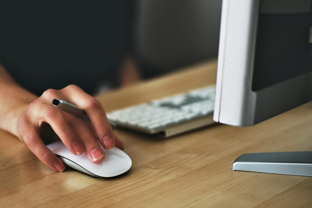 Detail showing the corner of a desktop computer, with a screen and a keyboard, and a hand holding a mouse.