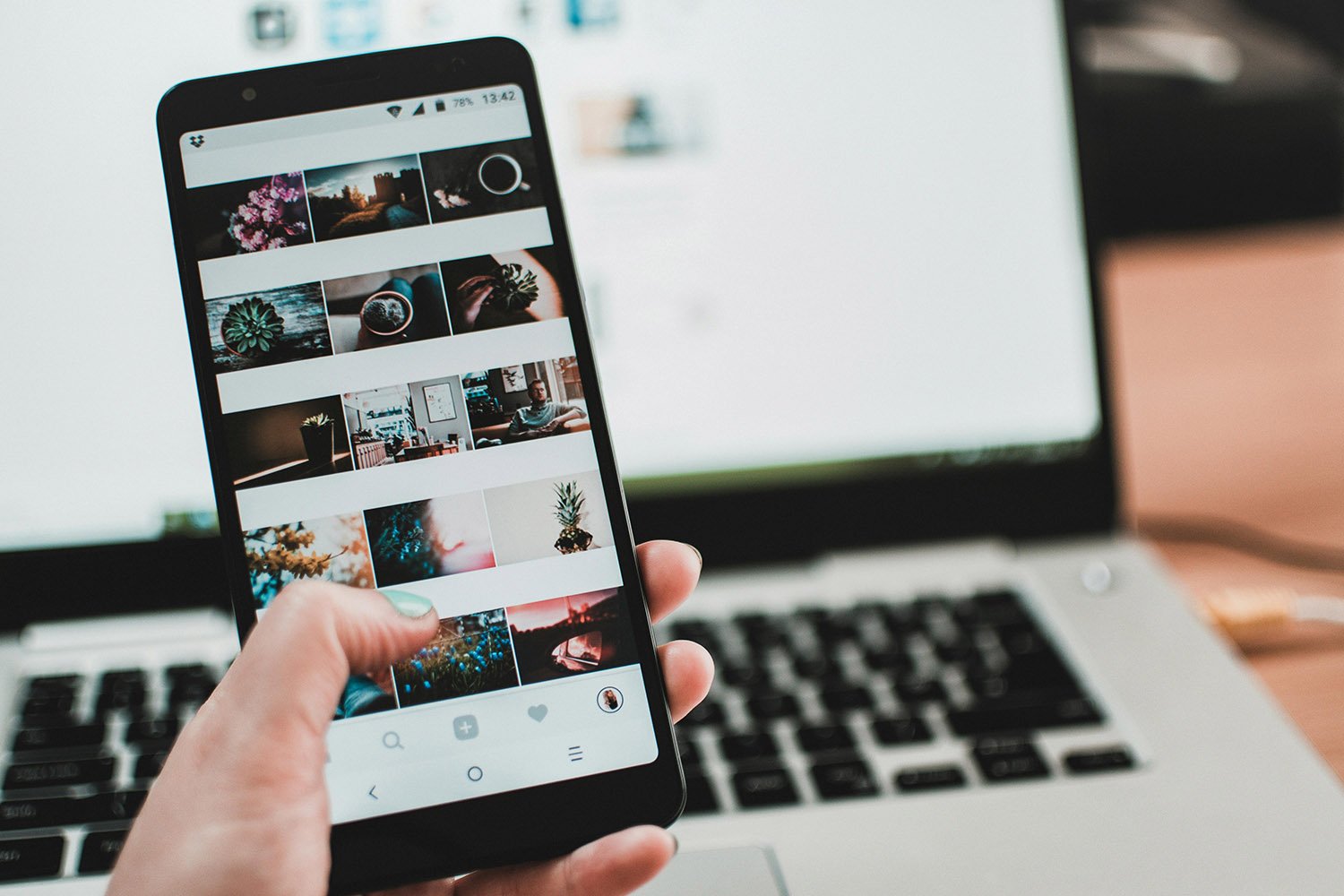 An iPhone with a range of photos, with in the background an open laptop.
