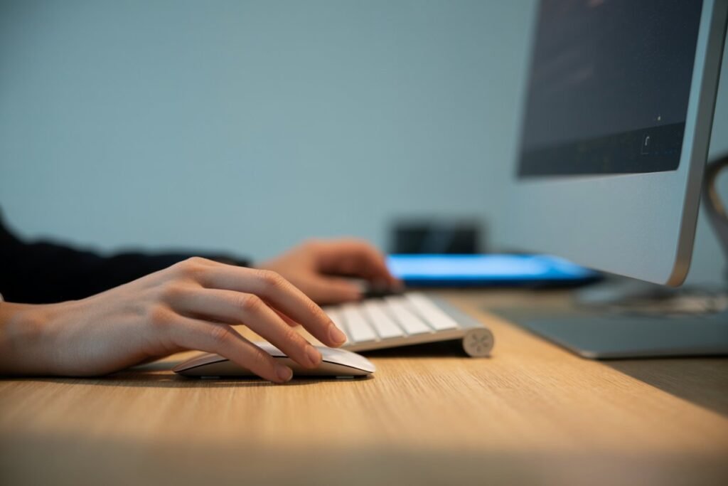 Detail showing the corner of a desktop computer, with a screen and a keyboard, and a hand holding a mouse.
